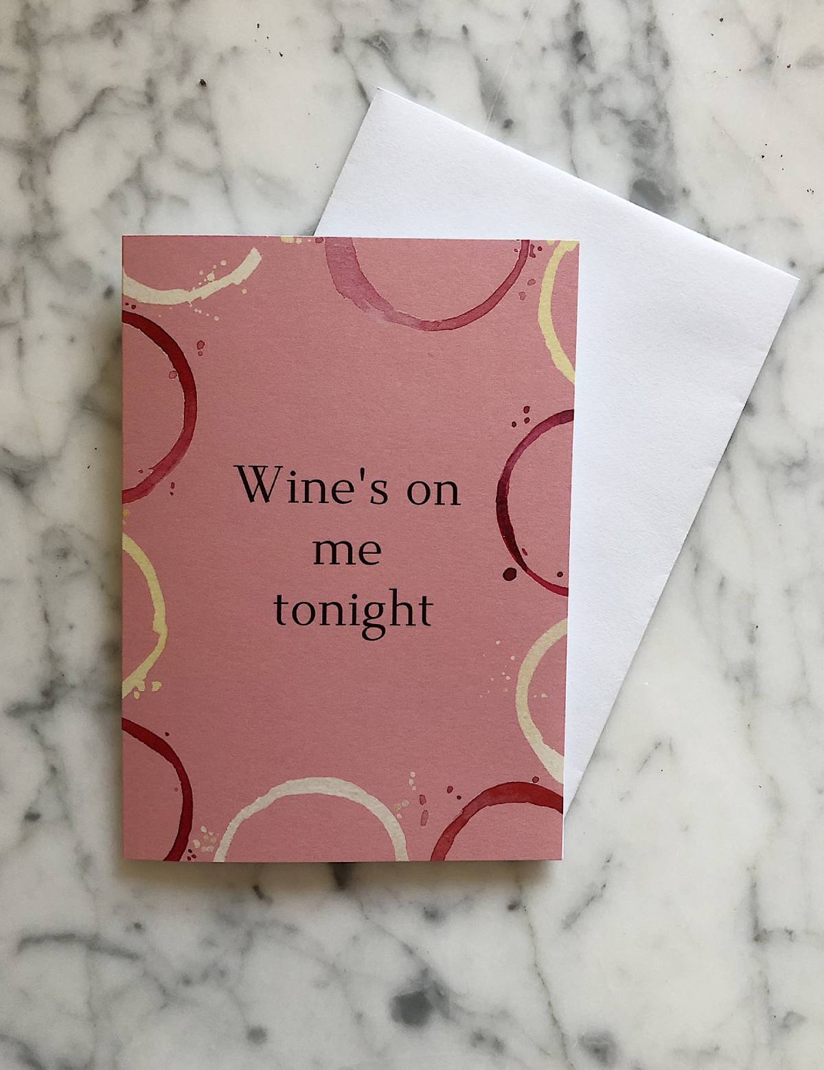 A pink card with an outline of various colored wine stains and the text "Wine's on me tonight"